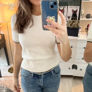 Vit ribbad topp med glitter detaljer - Säljer en superfin vit ribbad topp med korta ärmar och svarta detaljer vid ärmslut. Perfekt för en casual look eller att klä upp med accessoarer. Toppen är tight och passar bra till jeans eller kjol.