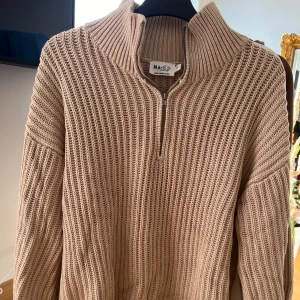 Beige stickad tröja från NA-KD - Säljer en superfin beige stickad tröja från NA-KD. Den har en dragkedja framtill och en hög krage som gör den perfekt för kyliga dagar. Tröjan är långärmad och har en mysig, ribbad struktur. Perfekt för höst och vinter!
