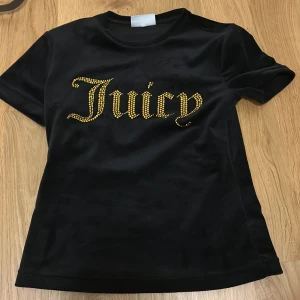 Svart t-shirt från Juicy Couture😎😎💘💘 - Snygg svart t-shirt från Juicy Couture med guldfärgad text på framsidan och sammetstyg. Perfekt för en trendig look med en touch av glamour.anvönd ett fåtal gånger och ser helt ny ut💕💕priset går att diskuteras💘💘