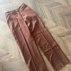 Bruna kostymbyxor - Snygga bruna kostymbyxor med hög midja och raka ben. Perfekta för en stilren look. Byxorna har diskreta fickor och en klassisk design. MADLADY 34/short