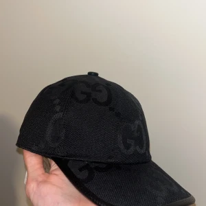 Svart keps från Gucci Size M - Snygg svart keps från Gucci med diskret GG-mönster. Justerbar rem baktill för perfekt passform. Tillverkad i Italien med högkvalitativt material.