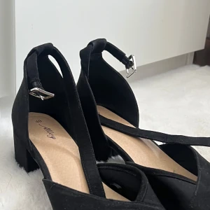 Svarta klackskor med remmar - Snygga svarta klackskor med remmar och spänne. Perfekta för en elegant look med en bekväm klackhöjd. Passar bra till både vardag och festliga tillfällen.
