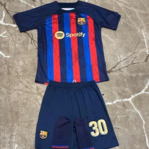 FC Barcelona fotbollströja med shorts - Snygg FC Barcelona tröja med shorts. Tröjan har rödblå ränder och korta ärmar, med sponsorlogga på framsidan och spelarnamnet 'Gavi' samt nummer 30 på baksidan. Perfekt för fans! 💙❤️