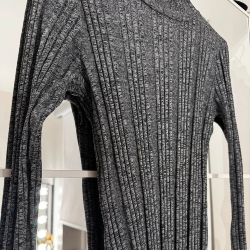 Snygg grå ribbad klänning med lång ärm och hög krage. Perfekt för kyligare dagar med sin stickade look. Klänningen har en figurnära passform som framhäver silhuetten.. Mekot.