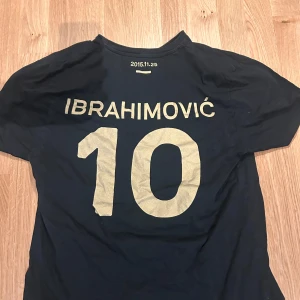 Svart t-shirt med Ibrahimović-tryck - Cool svart t-shirt med stort Ibrahimović-tryck och nummer 10 på baksidan. Framsidan har text med städer som Malmö, Amsterdam, Barcelona och Paris. Perfekt för fotbollsfans!
