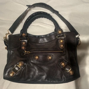 Intressekoll Svart Balenciaga city bag - Intressekoll på min svarta balenciaga city bag med guld detaljer. I bra skick, lite slitningar på handtagen, men annars fin. Inkluderar en liten plånbok och spegel. Inget kvitto eller dustbag. 