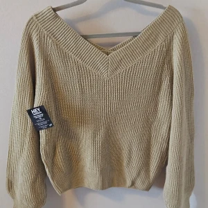 Beige stickad tröja från NLY Trend - Säljer en snygg beige ny stickad tröja från NLY Trend / Nelly med v-ringad hals och offshoulder-design. Mjukt och skönt material. Perfekt för en stilren och avslappnad look. Tröjan har långa ärmar och ribbade detaljer vid hals och ärmslut. Helt ny!