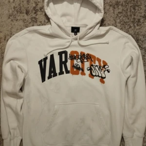 Vit hoodie från H&M med tryck - Säljer en vit hoodie från H&M med texten 'VAR CITY' i svart och orange graffiti-stil. Hoodien har en känguruficka och justerbar dragsko i huvan. Perfekt för en avslappnad stil!