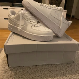 Vita Nike Air Force 1 - Säljer ett par klassiska vita Nike Air Force 1 sneakers. De har en stilren design med snörning och är tillverkade i syntetmaterial.dem är  I ny skick aldrig använda storlek 40 men lådan är skadad därför säljer jag billigt 