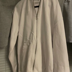 Vit hoodie med dragkedja - Säljer en stilren vit hoodie med dragkedja. Den har en klassisk design med huva och långa ärmar. Perfekt för en avslappnad look. Nypris: 449 skick 9/10