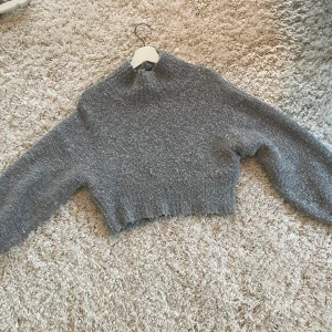 Grå stickad tröja från Monki - Säljer en mysig grå stickad tröja från Monki. Tröjan har en hög krage och är croppad med långa ärmar. 
