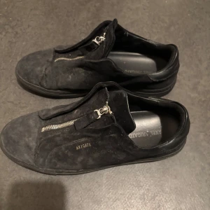 Svarta sneakers från Axel Arigato - Snygga svarta sneakers från Axel Arigato i mocka med dragkedja framtill. Perfekta för en stilren look.