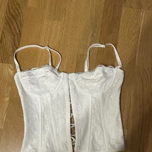 Vit korsett med spetsdetaljer - Elegant vit korsett med spetsdetaljer och snörning i ryggen. Axelbanden är justerbara för perfekt passform. Väldigt basic korsett me inga defekter kommer bara inte till någon användning👍🏼😊