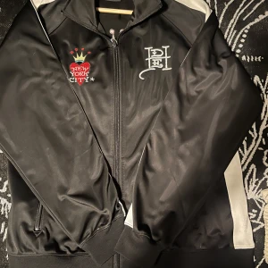 Ed Hardy jacka  - Snygg svart jacka med dragkedja och broderad New York City-design. Jackan har vita detaljer på ärmarna.