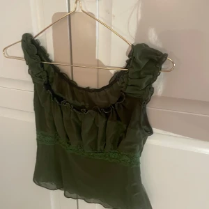 Grön ärmlös topp med volangdetaljer - Snygg grön ärmlös topp med volangdetaljer och spets. Perfekt för en somrig look. Toppen har en luftig passform och är gjord i ett lätt material.