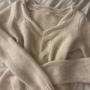 Beige stickad tröja - Mysig beige stickad tröja med v-ringning och ribbade detaljer. Perfekt för kyliga dagar.