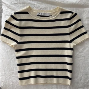 Randig kortärmad topp från Zara - Säljer en stilren randig topp från Zara i svart och beige. Den är kortärmad och har en klassisk rund halsringning. Perfekt för en avslappnad look. Den är använd en gång och är i nytt skick.
