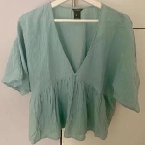 KORTÄRMAD TRÖJA FRÅN LINDEX  - Snygg ljusblå blus från Lindex med v-ringning och korta ärmar. Blusen har en luftig passform och ett lätt rynkat tyg som ger en avslappnad look. Perfekt för vår och sommar!