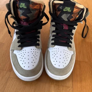 Nike Air Jordan sneakers med grå och vinröd detalj - Snygga Nike Air sneakers med en kombination av grå mocka och vita paneler. De har vinröda detaljer och svart snörning. Perfekta för en stilren look.