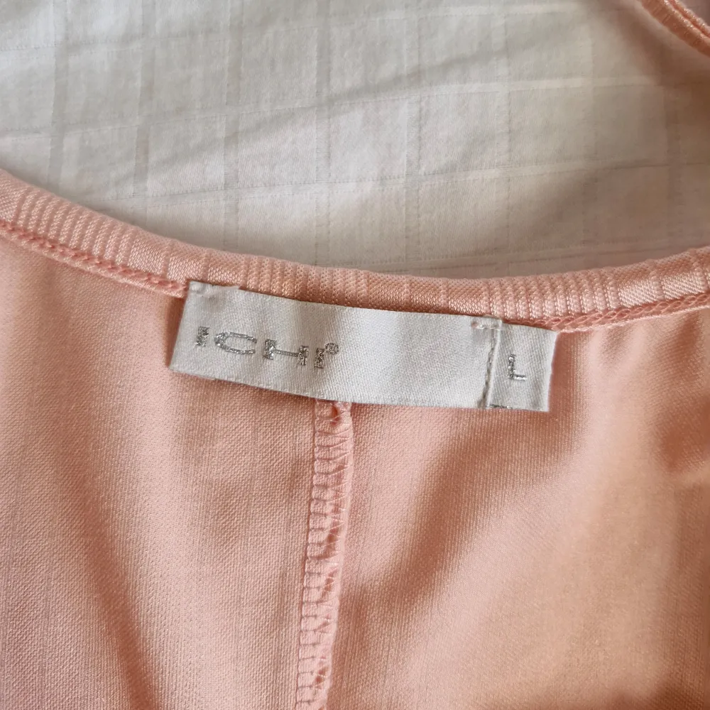 Säljer ett sött rosa linne från ICHI med tunna axelband och en liten rosett framtill. Linnet har ett elegant veckat mönster och är tillverkat i ett glansigt material som ger en lyxig känsla.. Yläosat.