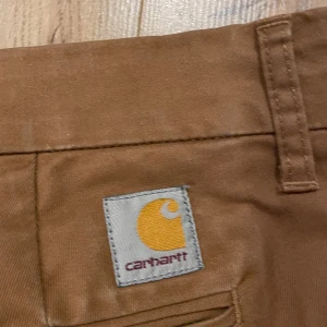 Carhartt byxor bruna - Säljer ett par bruna byxor från Carhartt. De har en klassisk design med en rak passform och är tillverkade i en slitstark bomullsblandning. Perfekta för en avslappnad stil.