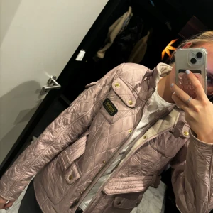 Gammal Rosa quiltad jacka från Barbour - Säljer en snygg gammal rosa quiltad jacka från Barbour International. Jackan har en bälte i midjan och flera fickor med knappar. Perfekt för höst och vår med sin stilrena design och praktiska detaljer. Storlek XXL i barn men känns som en storlek S!!!