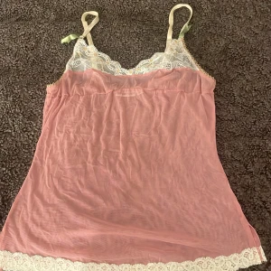 Rosa linne med spetsdetaljer från Gina Tricot - Säljer ett sött rosa linne från Gina Tricot med vackra spetsdetaljer i vitt och små blommor. Linnet har justerbara axelband och en luftig passform, perfekt för varma dagar.