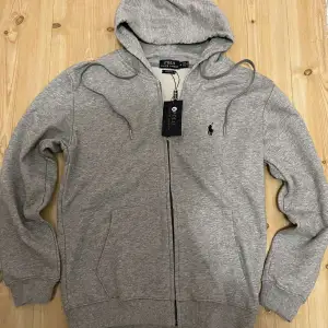 En riktig stilig ralph lauren zip hoodie i grå färg och storlek M. skicket på denna är helt ny och oanvänd. 