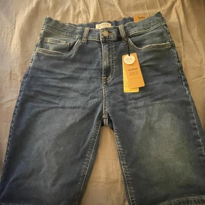 Blå jeansshorts från Lindex - Säljer ett par snygga blå jeansshorts från Lindex i storlek 170. De är i nyskick med etiketten kvar. Shortsen har en klassisk femficksdesign och stängs med knapp och dragkedja. Perfekta för sommaren! Aldrig använda endast testade