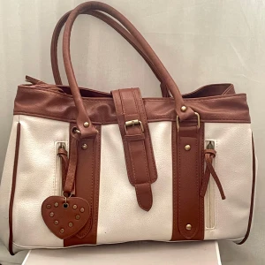 Gullig väska🐻👜 - Jätte gullig väska i färgen vit och brun. Den har en jätte gullig nyckelring som är ett hjärta! Den har tecken på användning på baksidan och inuti men det är inte något man lätt märker🫶🏻