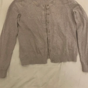 Beige kofta från HM - Säljer en enkel och stilren beige kofta från HM. Den har långa ärmar och knappar framtill. Perfekt för både vardag och lite kyligare dagar. Passar bra till både jeans och kjol. 🧥✨