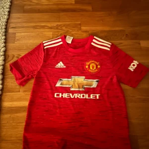 Manchester United hemma kit säsong 2020-2021 - Tröjan och shortsen har storleken 164, använd endast ett fåtal gånger. Skick: 8/10 skulle inte säga att det är något dåligt skick på varan men den jag använt cirka fem gånger. Köpare står för frakten. Modellen är 147 cm lång och väger 32 kg. 