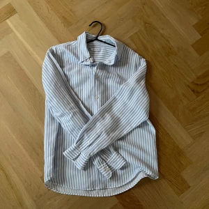 Skjorta - Säljer en stilren och klassisk randig skjorta från Zara. Den är vit med ljusblå ränder och har långa ärmar. Perfekt för både vardag och festliga tillfällen. Skjortan är i bomull och har en normal passform. Pris kan diskuteras 🤗