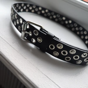 Svart bälte med silverdetaljer - Säljer ett coolt svart bälte med massor av silverfärgade nitar. Perfekt för att ge din outfit en edgy touch! Bältet har några små skavanker men förövrigt i bra skick. Passar både till jeans och klänning. Perfekt accessoar för att sticka ut!