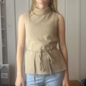 Beige ärmlös polotopp med knytband - Säljer en stilren beige ärmlös polotopp med knytband i midjan. Toppen har en elegant polokrage och är perfekt för både vardag och fest. Materialet känns mjukt och bekvämt, vilket gör den idealisk för vår och sommar. ❤️❤️❤️