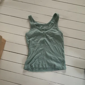 Grön ribbad linnetopp från 157 - Säljer en snygg grön ribbad linnetopp från 157. Den är i storlek M och är tillverkad av 60% bomull och 40% polyester. Toppen har knappar framtill och är perfekt för sommaren. Den är i bra skick och redo för en ny ägare!