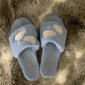 Blå fluffiga tofflor - Säljer ett par supermysiga blå tofflor med fluffigt material. De har en öppen tå-design och en hårdare sula. Tofflorna har också söta vita moln som detalj❤️☁️ Tofflorna passar mig som vanligtvis har storleken 35-36 i skor.