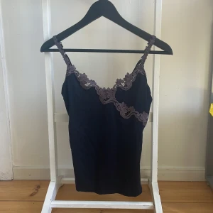 Svart linne från Lindex - Säljer ett snyggt svart linne från Lindex, storlek S (36/38). Det är gjort av 80% polyamid och 20% elastan, vilket gör det stretchigt och bekvämt. Linnet har spetsdetaljer längs halsringningen och justerbara axelband. Frakt: runt 30kr (icke spårbar)