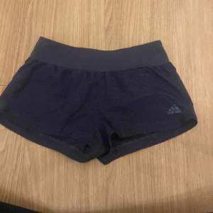 Säljer ett par marinblå träningsshorts från Adidas. De är i nyskick och har en tight passform. Perfekta för träning eller löpning. Shortsen har en bred elastisk midja för extra komfort.