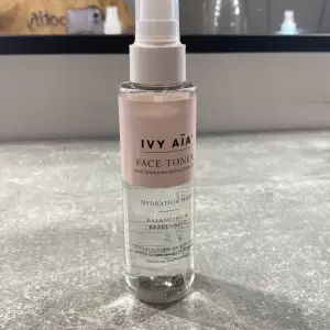 Säljer en face toner från Ivy Aïa med hyaluronsyra och niacinamid. Denna toner är perfekt för att balansera och fräscha upp huden. Den kommer i en genomskinlig plastflaska med en rosa etikett och vit spraypump. Flaskan innehåller 120 ml och är tillverkad av 100% återvunnen plast.