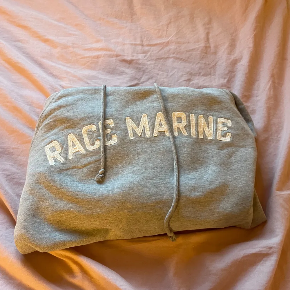 Säljer en grå hoodie från Race Marine. Den är supermjuk och bekväm, perfekt för kyliga dagar. Hoodien har en stor ficka på magen och en justerbar huva med dragsko. Texten 'RACE MARINE' är tryckt på bröstet i vitt. Passar perfekt för en avslappnad stil eller för att mysa hemma. 🧥. Tröjor & Koftor.