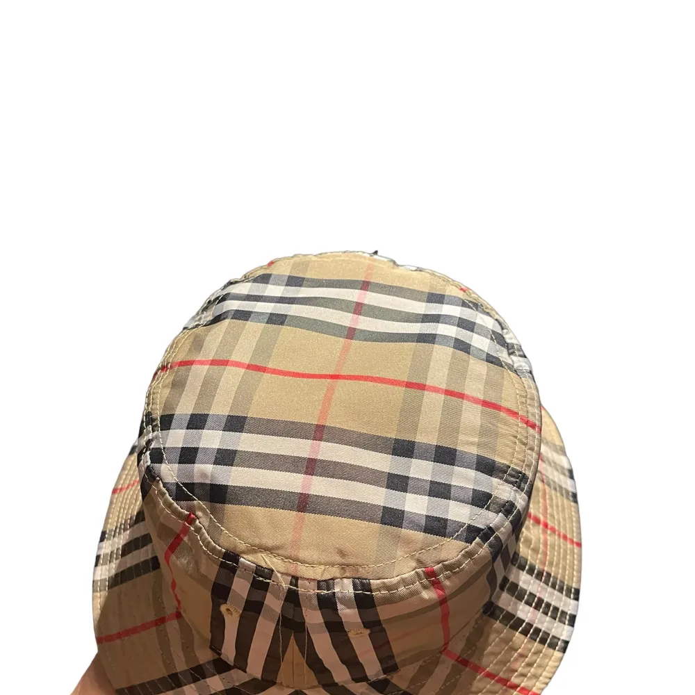 Säljer en riktigt fet burberry bucket hat i beige, svart, röd och vit. Hatten har ett klassiskt rutmönster och är perfekt för sommaren. Den är i nyskick och passar både killar och tjejer. Materialet känns som bomull och den har en normal passform.. Accessoarer.