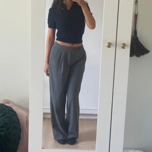 Grå kostymbyxor - Säljer ett par grå kostymbyxor i storlek dam M. Byxorna är högmidjade och har en loose passform. De har en knappdetalj i midjan och är perfekta för både vardag och fest. Materialet känns som bomull och polyester, vilket gör dem bekväma och stiliga.