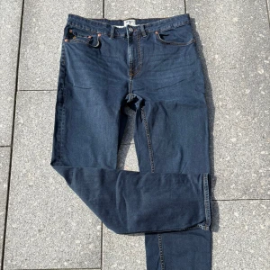 Morris blå jeans straight fit - Snygga blå jeans från Morris i klassisk straight fit med fem fickor och kontrastsömmar. Jeansen har en mörk tvätt, läderpatch bak och diskret logga på myntfickan. Perfekta för dig som gillar stilrena och tidlösa jeans.