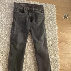 Svarta Replay jeans slim fit - Snygga svarta jeans från Replay med klassisk femficksdesign och diskreta slitningar. Jeansen har smal passform och raka ben, perfekt för en clean och stilren look. Materialet är mjukt och stretchigt för extra komfort.