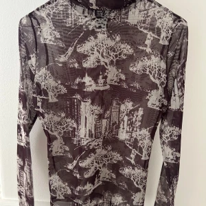 Brun mesh polotopp med stadsmotiv - Säljer en brun transparent polotopp med lång ärm och stadsmotiv i grått. Toppen är från Lindex
