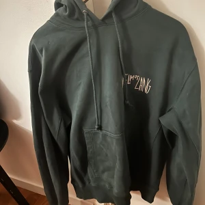 Mörkgrön Helmut Lang hoodie med print - Säljer en mörkgrön hoodie från Helmut Lang i 100% bomull. Tröjan har huva med snörning, stor ficka framtill och grafiskt tryck på ryggen. Tröjan är i väldigt bra skick