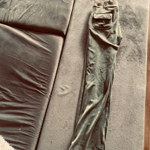 Gröna velourbyxor Juicy Couture XS - Snygga ljusgröna velourbyxor från Juicy Couture i storlek XS. Byxorna har bred resår i midjan, raka ben med lätt bootcut och stora fickor framtill med knappdetalj. Perfekta för en chill och trendig look.