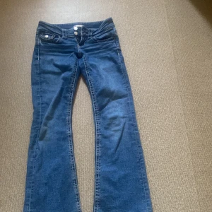 Blå bootcut jeans Gina Tricot 146 - Snygga blå jeans från Gina Tricot i storlek 146. Modellen har bootcut-ben, klassisk femficksdesign och dubbla knappar i midjan. Jeansen är tillverkade i ett mjukt denimtyg och har en cool, tidlös look.