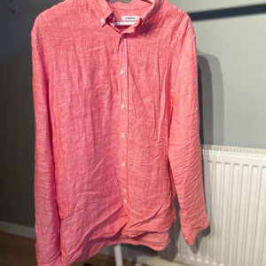 Rosa linneskjorta från J.Lindeberg - Säljer en snygg rosa skjorta från J.Lindeberg i luftigt linne. Skjortan har klassisk krage, vita knappar och lång ärm. Perfekt för dig som gillar en avslappnad men stilren look. Passformen är normal och materialet känns riktigt fräscht.